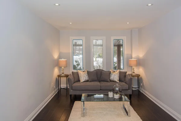Tilman Circle: Living-room sofa and glass coffee table beside three windows