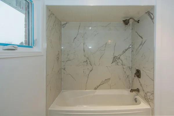 Tilman Circle: Bathtub with pale marble-patterned tile surround
